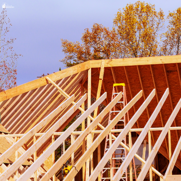 Wooden roof framing under construction with beams and ladder showing early stages of exterior home construction.