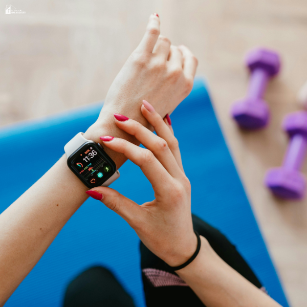 Person checking a smartwatch on a yoga mat beside dumbbells while using wearables during intense workouts.