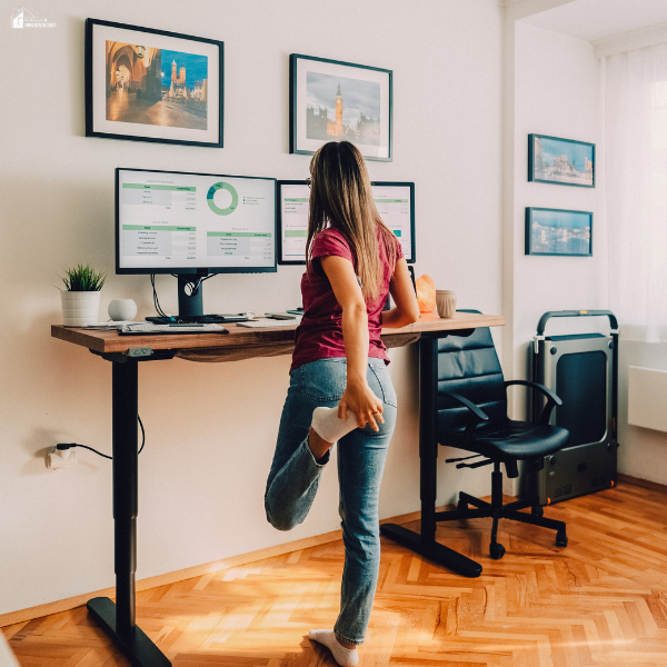 Woman stretching beside an adjustable standing desk workspace, showing ergonomic comfort and desk setup for shorter users.