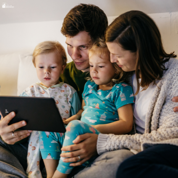 Parents sitting with young children using a tablet together, showing family supervision and safe online habits at home.