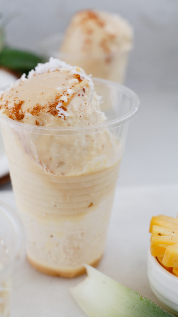 Creamy Limber de Coco y Piña served in a clear cup topped with shredded coconut and cinnamon, with fresh pineapple beside it.