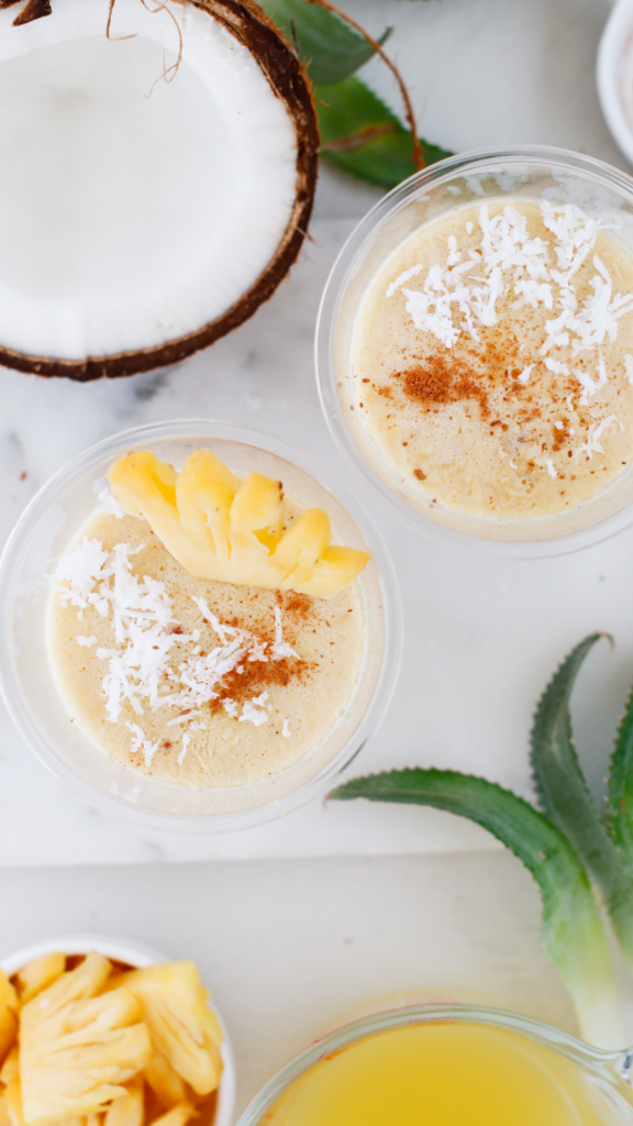 Two cups of Limber de Coco y Piña topped with coconut, cinnamon, and pineapple on a bright tropical tabletop.