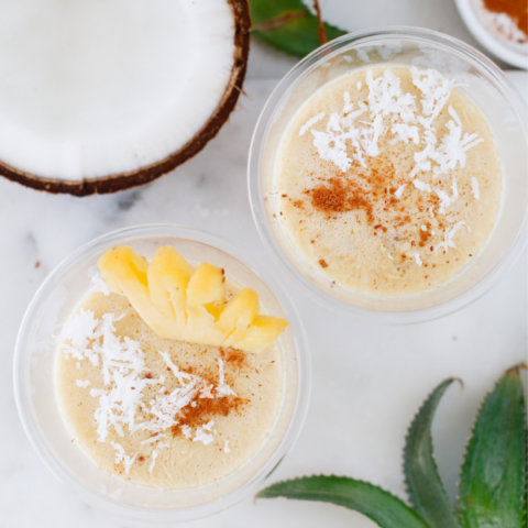 Two cups of Limber de Coco y Piña topped with coconut, cinnamon, and pineapple on a bright tropical tabletop.