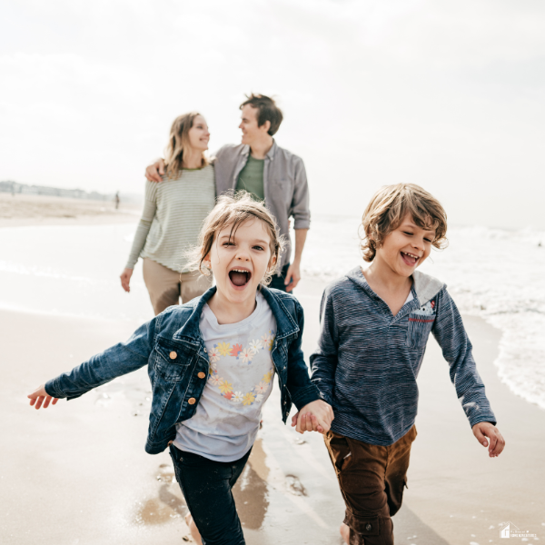 Two children running along the beach with parents in the background, showing family bonding and enjoying a safe and fun travel experience.