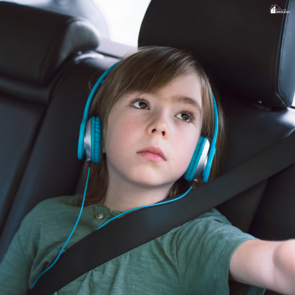 Child sitting in a car seat wearing headphones and a seatbelt, representing road trip safety, comfort, and entertainment for kids during travel.