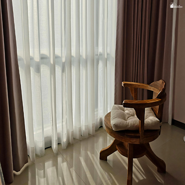 Sunlit room with sheer curtains and layered drapes beside a wooden chair, showcasing soft furnishings and window styling ideas.