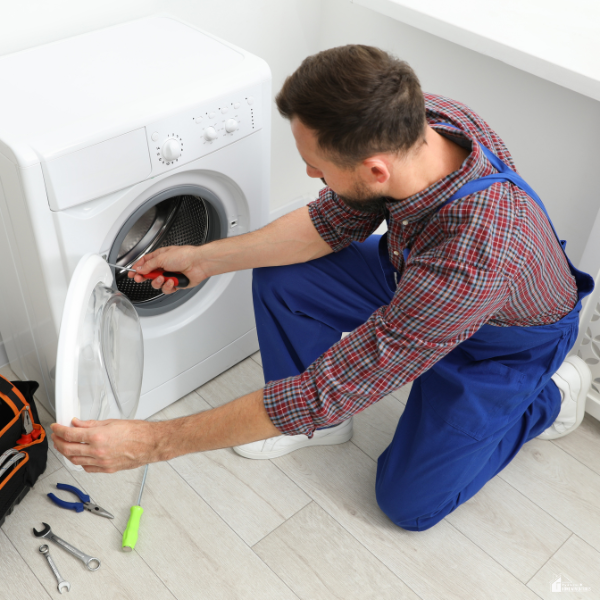 Man repairing a washing machine at home, showing practical home habits that help maintain appliances and reduce household stress.