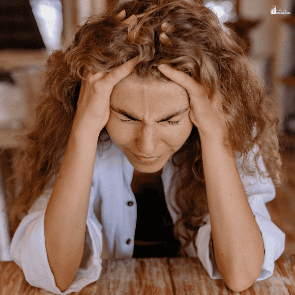 Stressed homeowner holding head while dealing with overwhelming home repair issues and delayed maintenance problems.