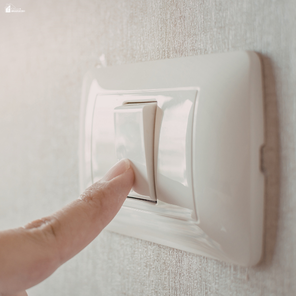 Finger pressing a wall light switch, representing electrical systems that may click, buzz, or make unusual household sounds.