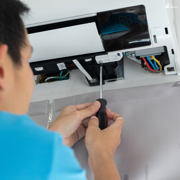 Person using a screwdriver to fix an air conditioning unit, showing a risky DIY repair that can lead to bigger problems if done incorrectly.