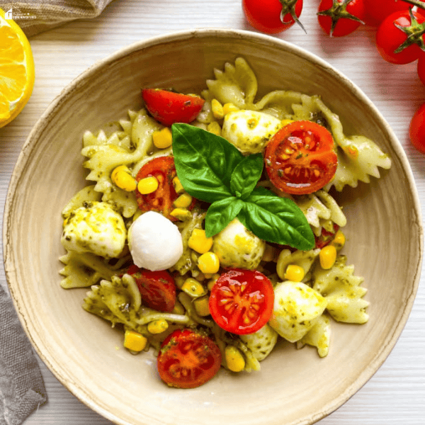 Fresh bowtie pasta salad with pesto, cherry tomatoes, mozzarella pearls, corn, and basil served in a bowl as one of the best summer pasta salad recipes for 2026.
