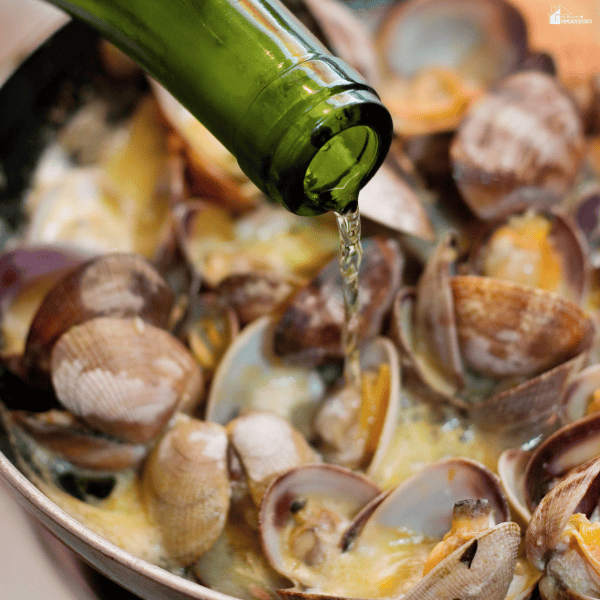 White wine being poured into a seafood dish while cooking to add flavor to clams and shellfish in a skillet.