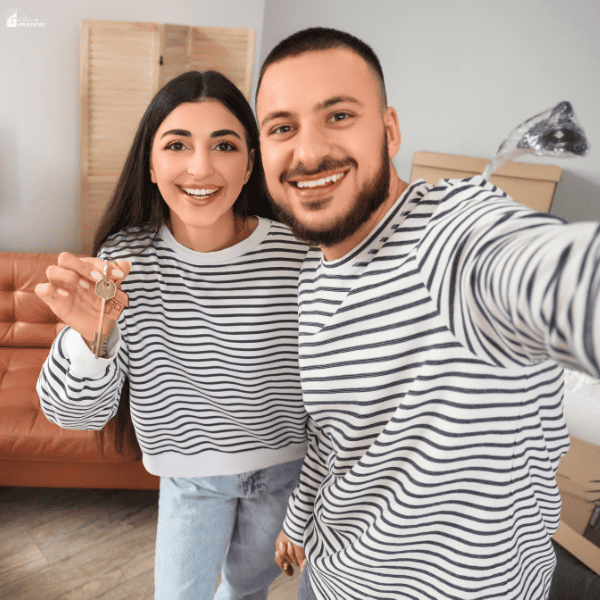 Smiling couple holding house keys inside a new home after moving into a smaller living space.