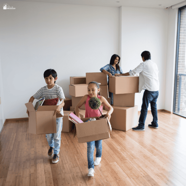 Family carrying moving boxes into a new home while children help unpack during a household move.