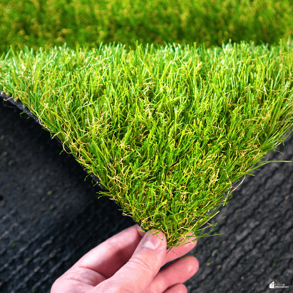 Close-up of synthetic grass material being held by hand to show texture and thickness for backyard landscaping projects.