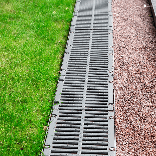 Outdoor drainage system installed beside green turf and gravel to support proper water flow in artificial grass landscaping.