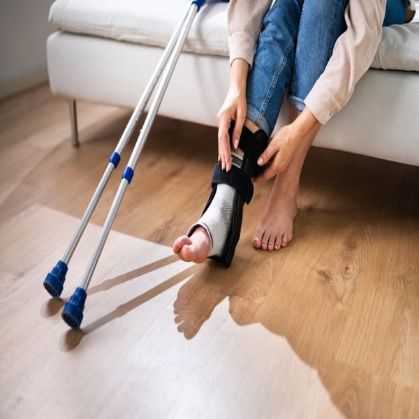Person wearing an ankle brace and using crutches at home after an injury that affects daily life and financial stability.