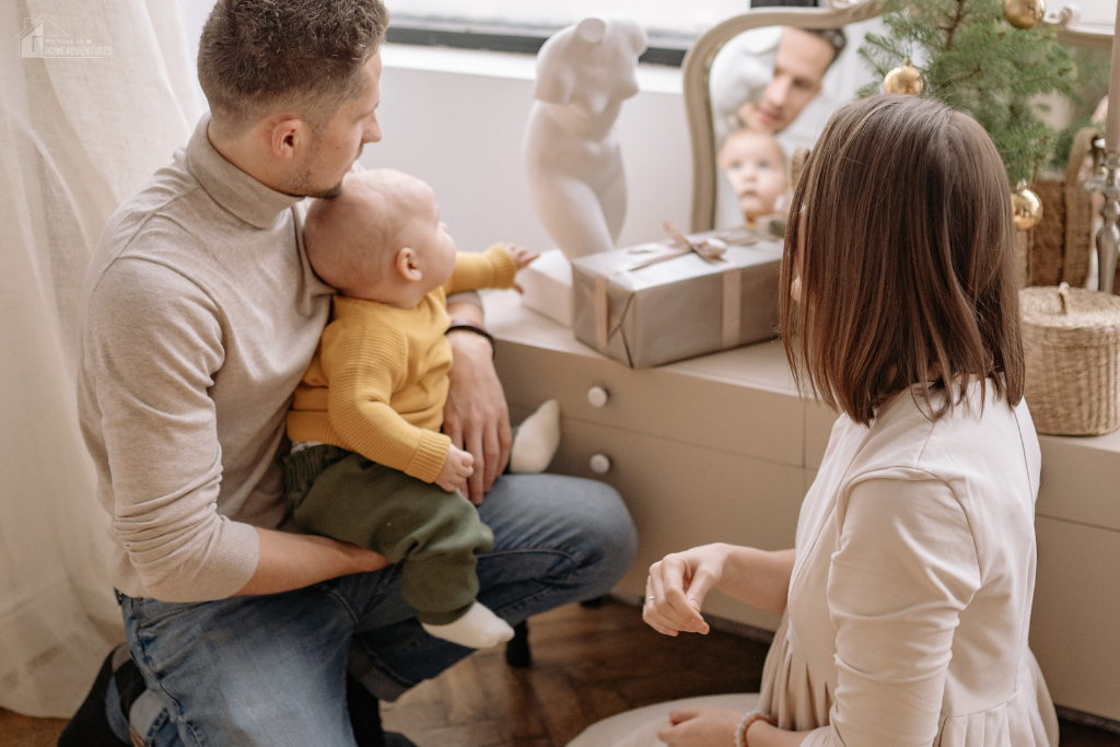 Family at home with parent holding baby and child nearby, showing everyday family life and routines in a comfortable, lived-in space.