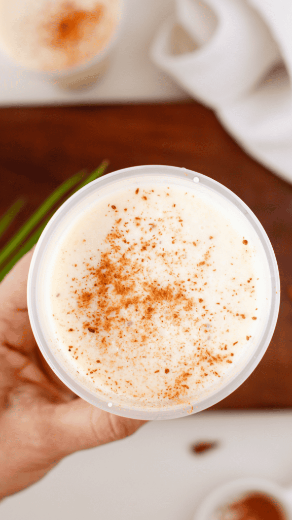 Hand holding a creamy tres leches limber topped with cinnamon in a plastic cup.