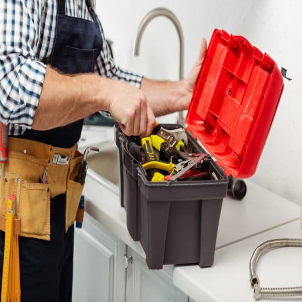 Home repair professional organizing plumbing tools in a kitchen as part of smart home maintenance habits that improve everyday comfort.