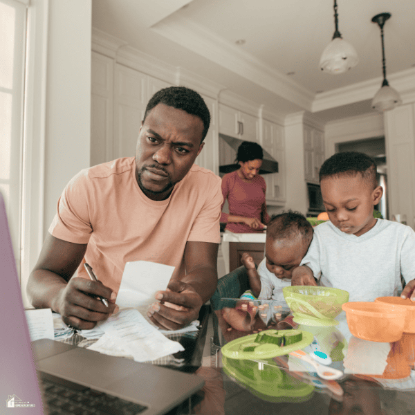 Parent reviewing household expenses at the kitchen table while managing childcare responsibilities and a family budget.
