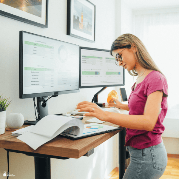 Professional using a standing desk workstation while reviewing documents and digital reports, illustrating healthy workplace habits and ergonomic office practices.