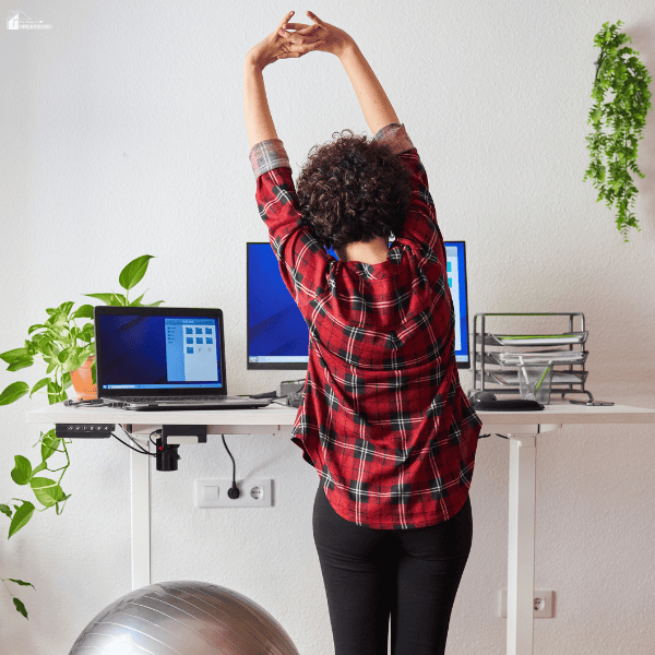 Office worker stretching at a standing desk setup, highlighting the importance of movement breaks and healthier work habits during the workday.