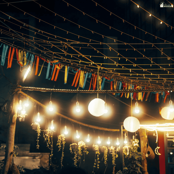 Outdoor gathering space decorated with hanging lights, lanterns, and colorful streamers to create a festive party backdrop.