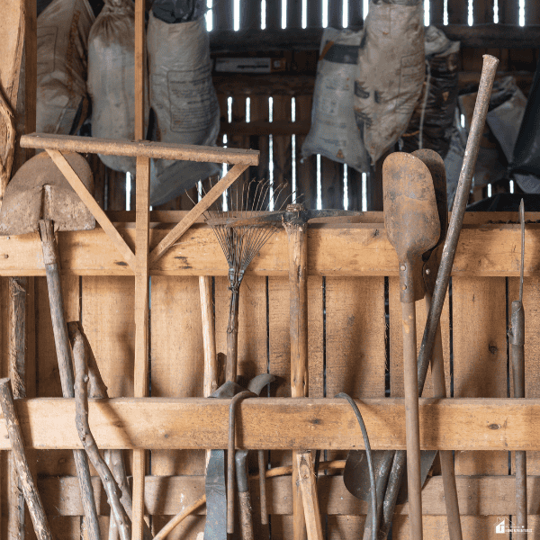 Garden tool storage area featuring rakes, shovels, and other hand tools neatly arranged on a wooden rack inside a shed.