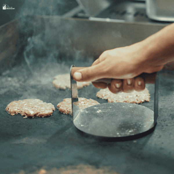 Smash burgers cooking on a griddle BBQ while a press creates a crisp sear on the flat-top surface.