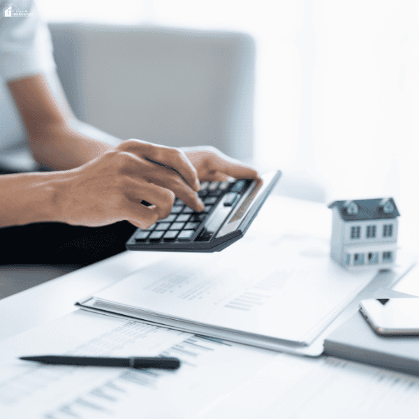 Person using a calculator beside property paperwork and a model house, illustrating cost segregation planning for real estate tax savings.