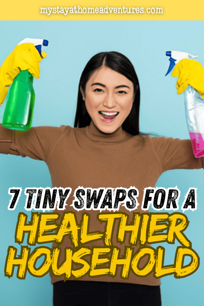 A smiling woman wearing cleaning gloves holds two household cleaning spray bottles, representing safer choices for maintaining a healthier home.