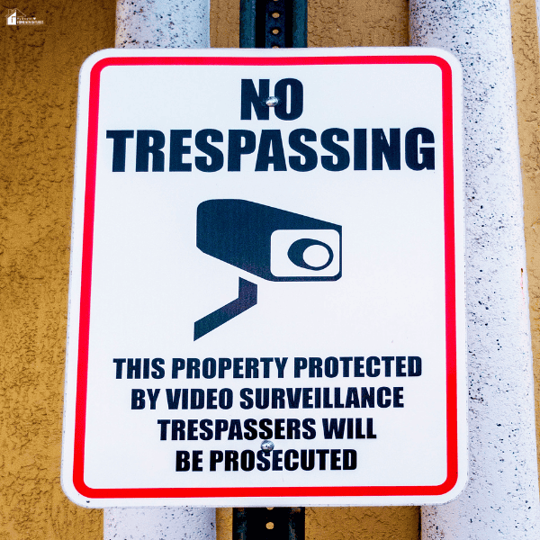Home surveillance warning sign displayed on an exterior wall, emphasizing the use of security cameras and property protection measures.