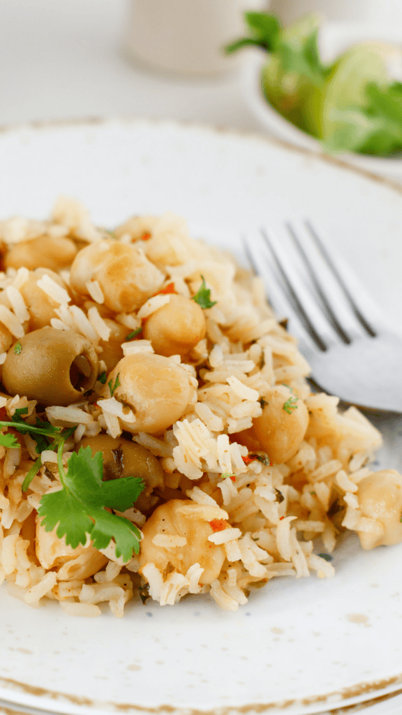 Close-up of Puerto Rican arroz con garbanzos served on a white plate with chickpeas, green olives, fresh cilantro, and a fork.