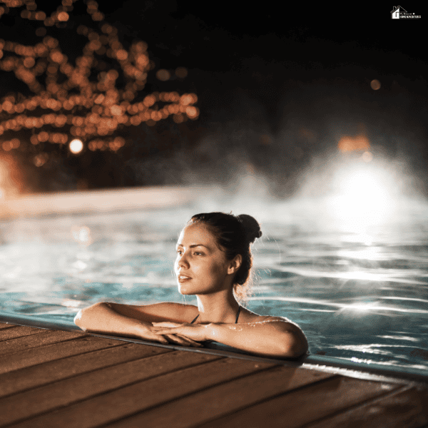 Person relaxing in a heated outdoor swimming pool at night, illustrating the comfort and extended use provided by a pool heating system.