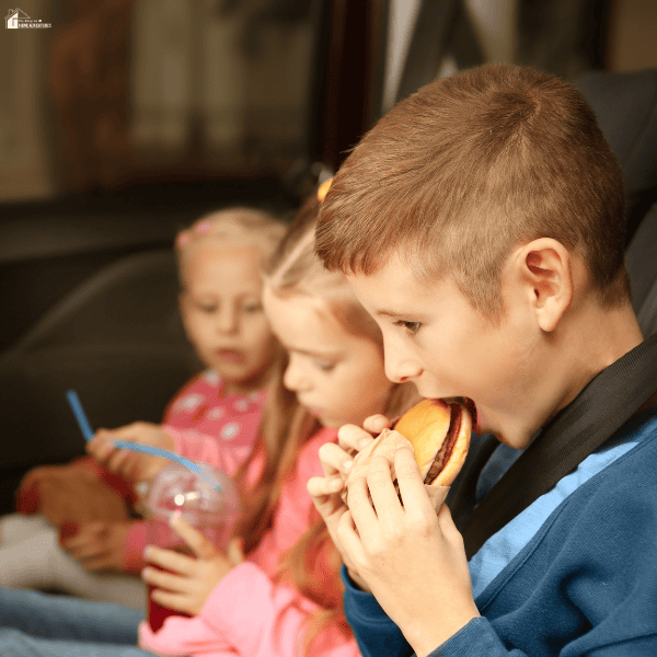 Children eating snacks in the back seat during a family road trip, highlighting simple ways to save money on travel meals.