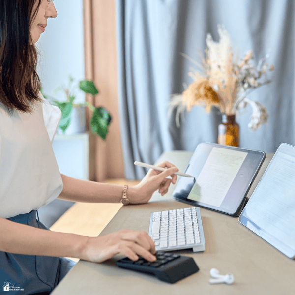 Woman working from a home office using digital tools and a calculator, representing flexible and profitable home business opportunities.
