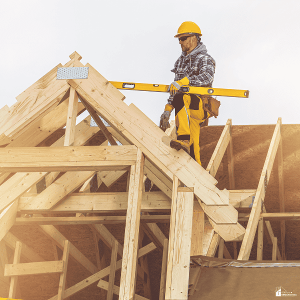A construction worker measures the roof framing of a house during a major exterior home improvement project.