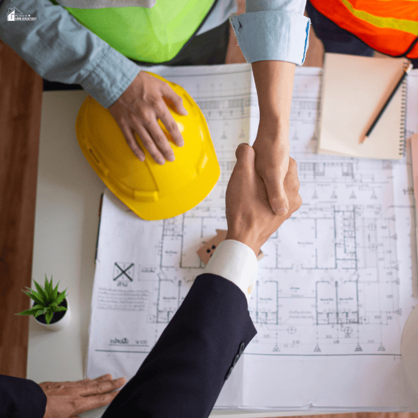 Homeowners and contractors review building plans and shake hands before starting an exterior renovation project.