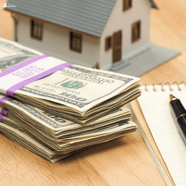 Stack of cash beside a model house represents situations where a cash home sale may be a practical option for Chicago homeowners.