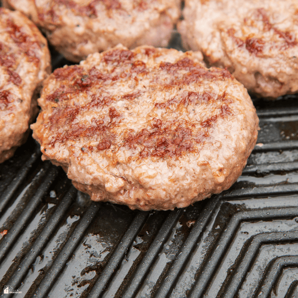 Juicy burger patties cooking on a hot outdoor griddle with browned surfaces and visible grill marks.