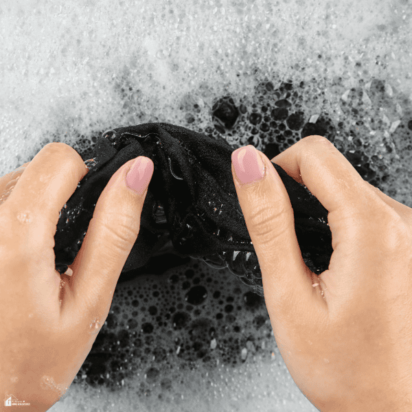 Hands gently washing a delicate black garment in soapy water as part of proper garment care for protecting fine fabrics and extending clothing life.