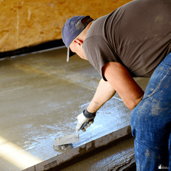 A worker smooths freshly poured concrete with a hand trowel to create an even and polished flooring surface.