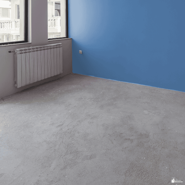 An empty room features a simple unfinished concrete floor beside a blue accent wall, showing a budget-friendly flooring option.