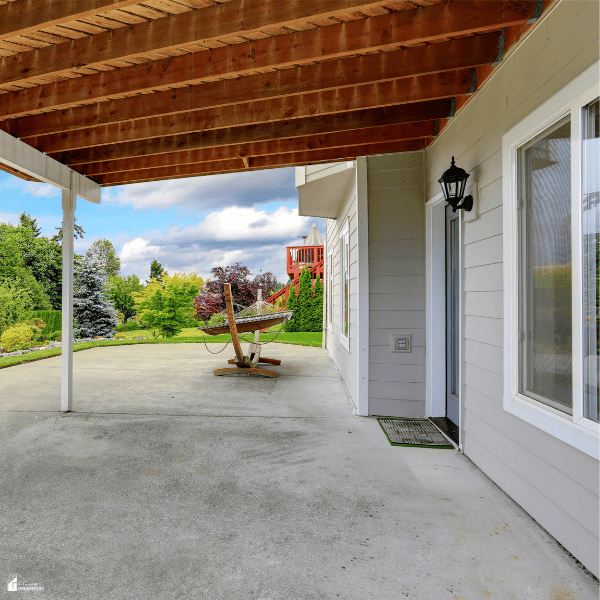 Covered backyard patio with exposed wooden beams and an open yard area that provides shade for more comfortable outdoor dining.