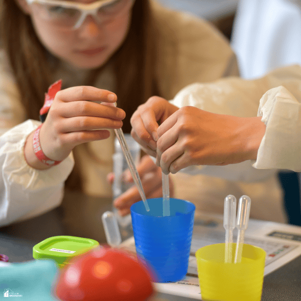 A child uses droppers and simple materials to complete a hands-on kitchen chemistry experiment while wearing safety goggles.