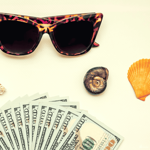 Travel savings, cash, sunglasses, and beach items arranged together to represent budgeting for an affordable dream vacation.