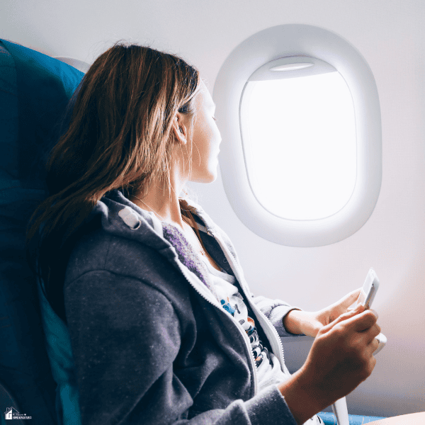 A traveler looks out an airplane window while holding a phone, representing affordable travel planning and budget-friendly trips.