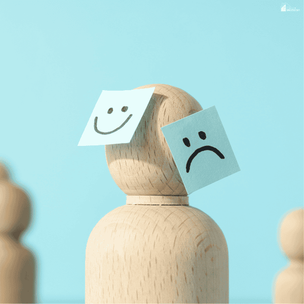 Wooden figure with happy and sad facial symbols representing changing emotions and the importance of mental health awareness.