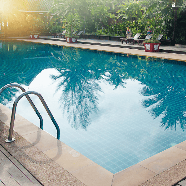 Finished backyard pool remodel featuring clear blue water, updated pool decking, a metal ladder, and landscaped surroundings.